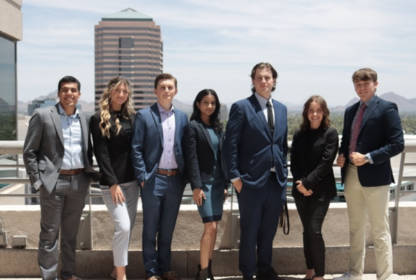 A group of students in business attire pose with a city skyline in background