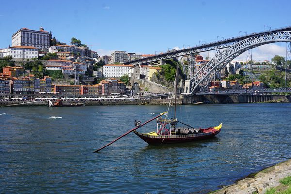 A boat floats on a river with Portuguese architecture dotting the hillside in the background