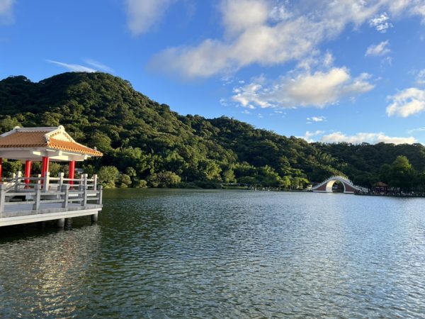 A deck with traditional-style architecture looks out on water and green mountains